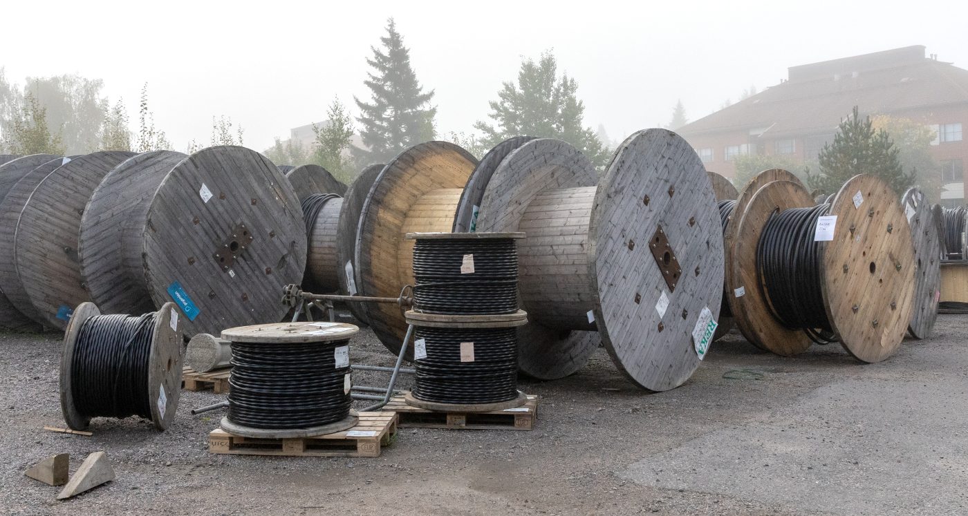 Puisia erikokoisia kaapelikeloja hiekkakentällä. Taustalla sumuinen maisema.