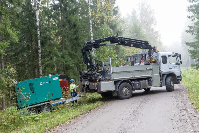 UVR:n kuorma-auto peruuttaa metsään perässään vihreä perävaunu.