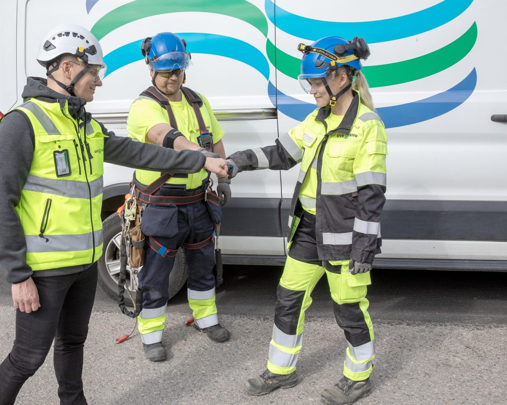 Kolme UVR:n ammattilaista turvavarusteissaan tekee nyrkkitervehdyksen hyvän yhteistyön merkkinä UVR:n auton edessä.
