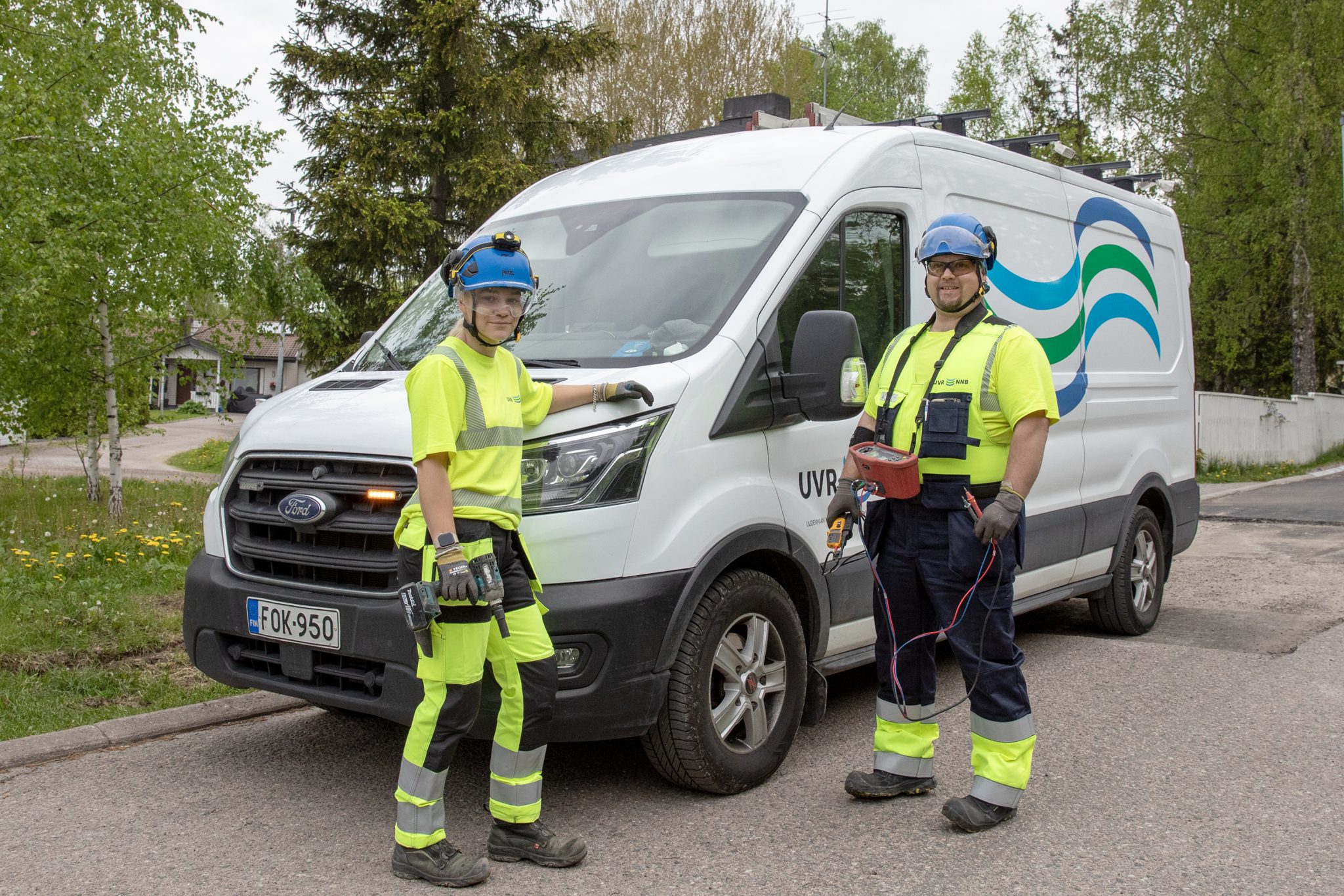 UVR:n kaksi työntekijää seisovat työvaatteissa työvälineet kädessä pakettiauton edessä.