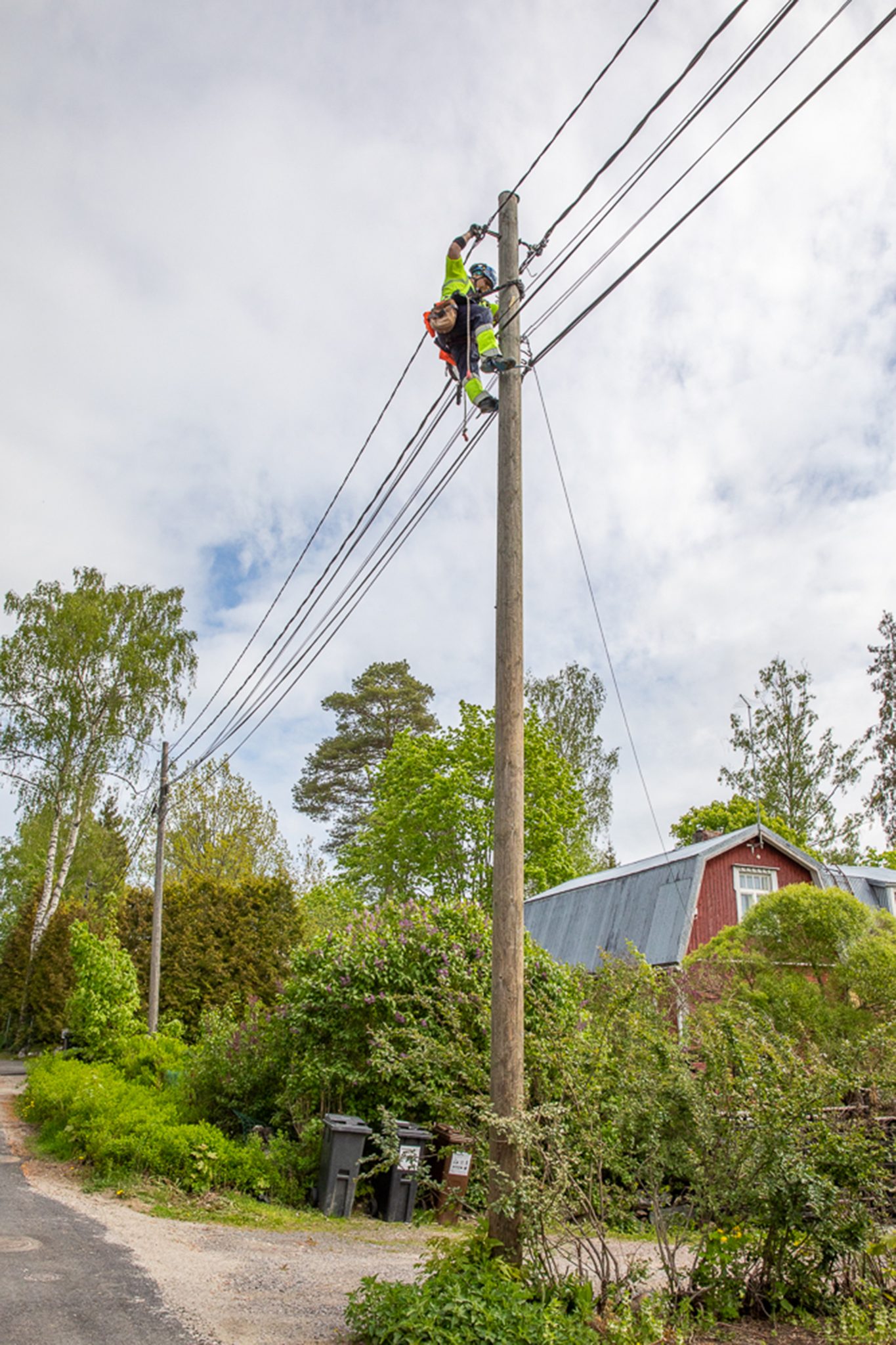Metsäinen asuinalue, punainen puinen asuintalo, jonka vieressä on sähköpylväs ja sähkölinja.