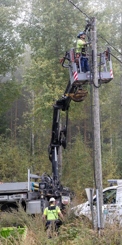 UVR:n ammattilaiset huoltamassa valaisinpylvästä maastossa. Nosturi ja UVR:n huoltoauto.
