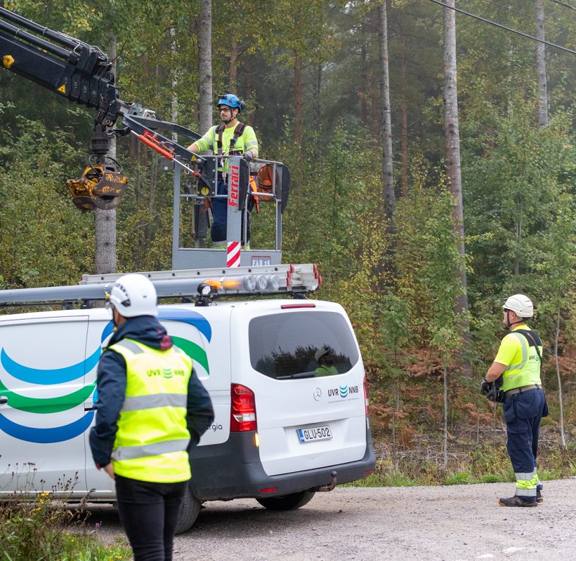 Yksi työntekijä henkilönostimessa, toinen käyttää nostinta. Yksi henkilö selin huoltoautomme edessä.